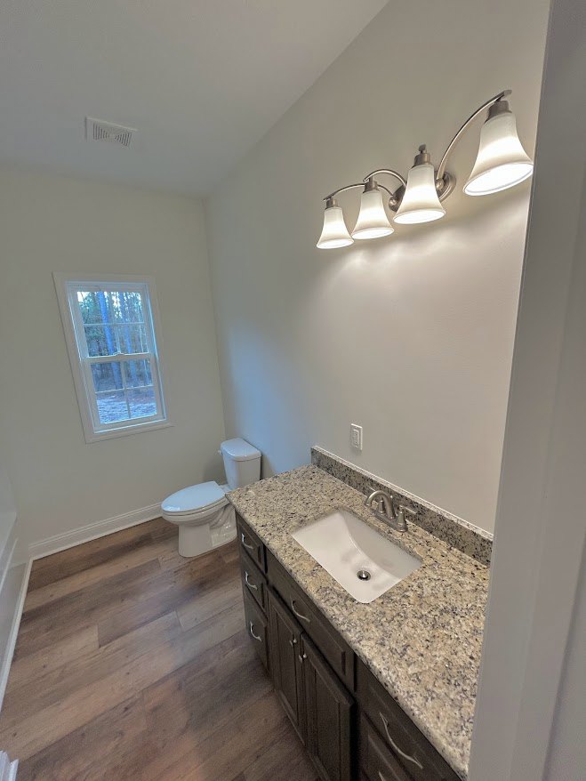 Marble countertop vanity with white sink and silver faucet, adjacent toilet, tiled walls, window overlooking trees, three-light fixture above mirror