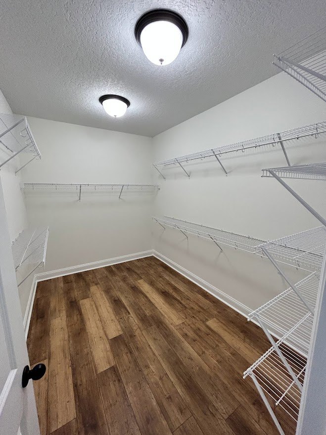 Hardwood floor with natural wood grain, white shelves featuring metal rods and hooks, white trim along baseboards, plaster walls, ceiling-mounted light fixture