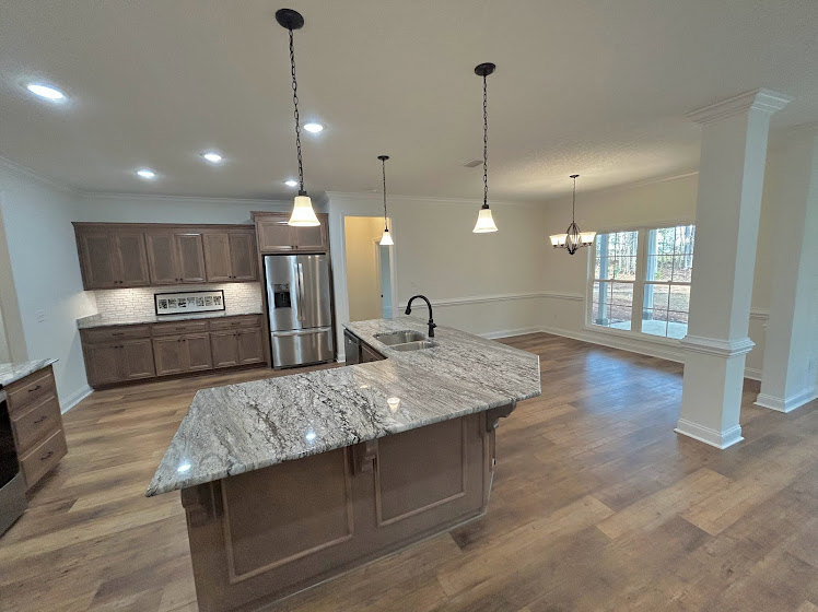 Spacious kitchen featuring a large central island with stone countertop, tile flooring, white cabinetry, stainless steel refrigerator, and pendant lighting above