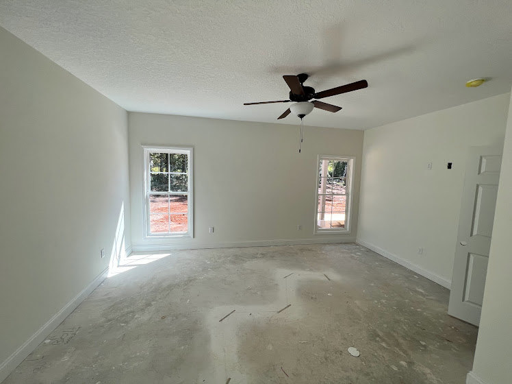 Ceiling fan with light fixture mounted on plaster ceiling, multiple windows along one wall, neutral painted walls, hardwood floor