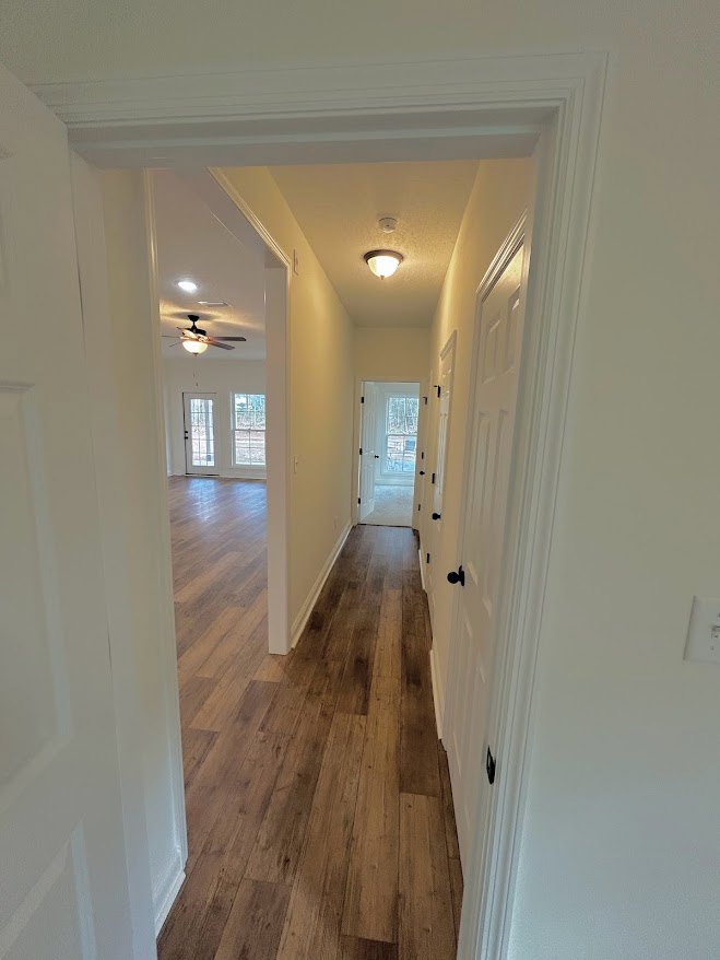 Hallway with white plaster walls, hardwood flooring, and a white door featuring glass panes and black knobs