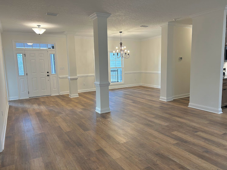 Wood flooring and white columns in a spacious room with white walls and a blue-trimmed window