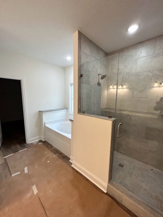 Bathroom featuring a frameless glass shower enclosure, freestanding white bathtub, marble tile flooring, and smooth white plaster walls.