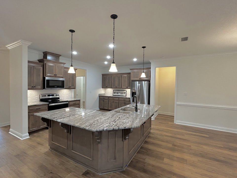 Spacious kitchen featuring a large marble island, stainless steel appliances including microwave, refrigerator, stove, and oven, white cabinetry, light fixtures on white walls, and