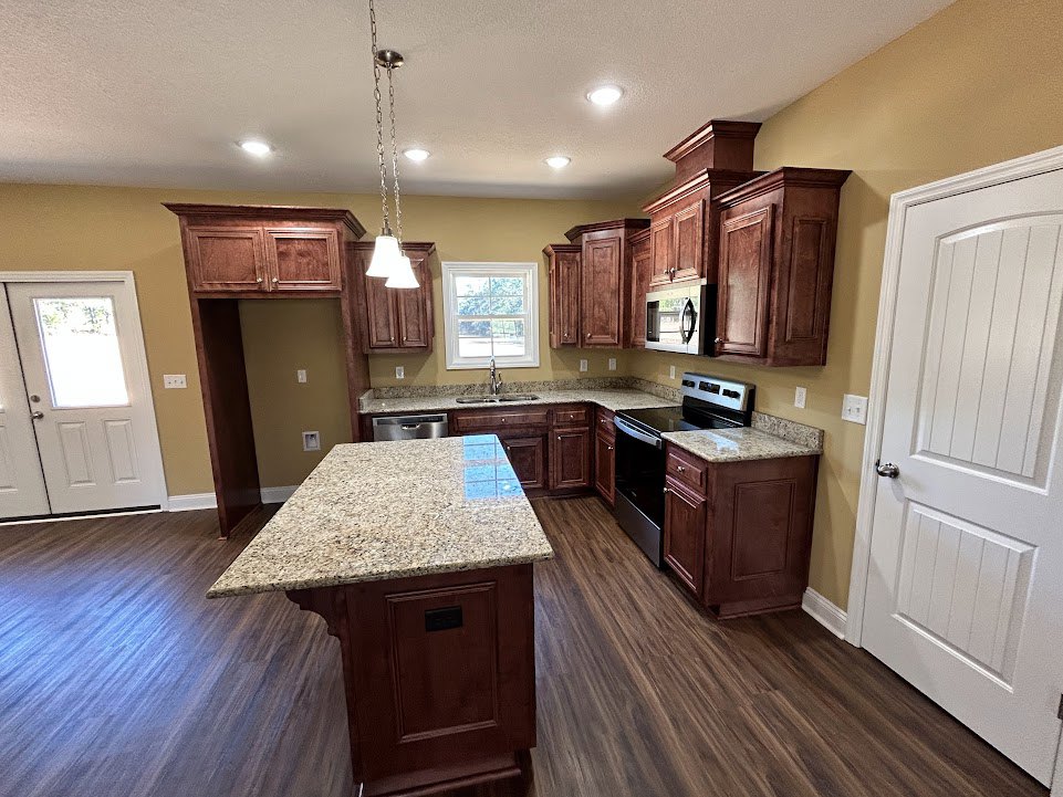 Kitchen with granite countertops, wood flooring, white cabinetry, stainless steel appliances, kitchen island with marble top, window with white frame, and close-up of a door