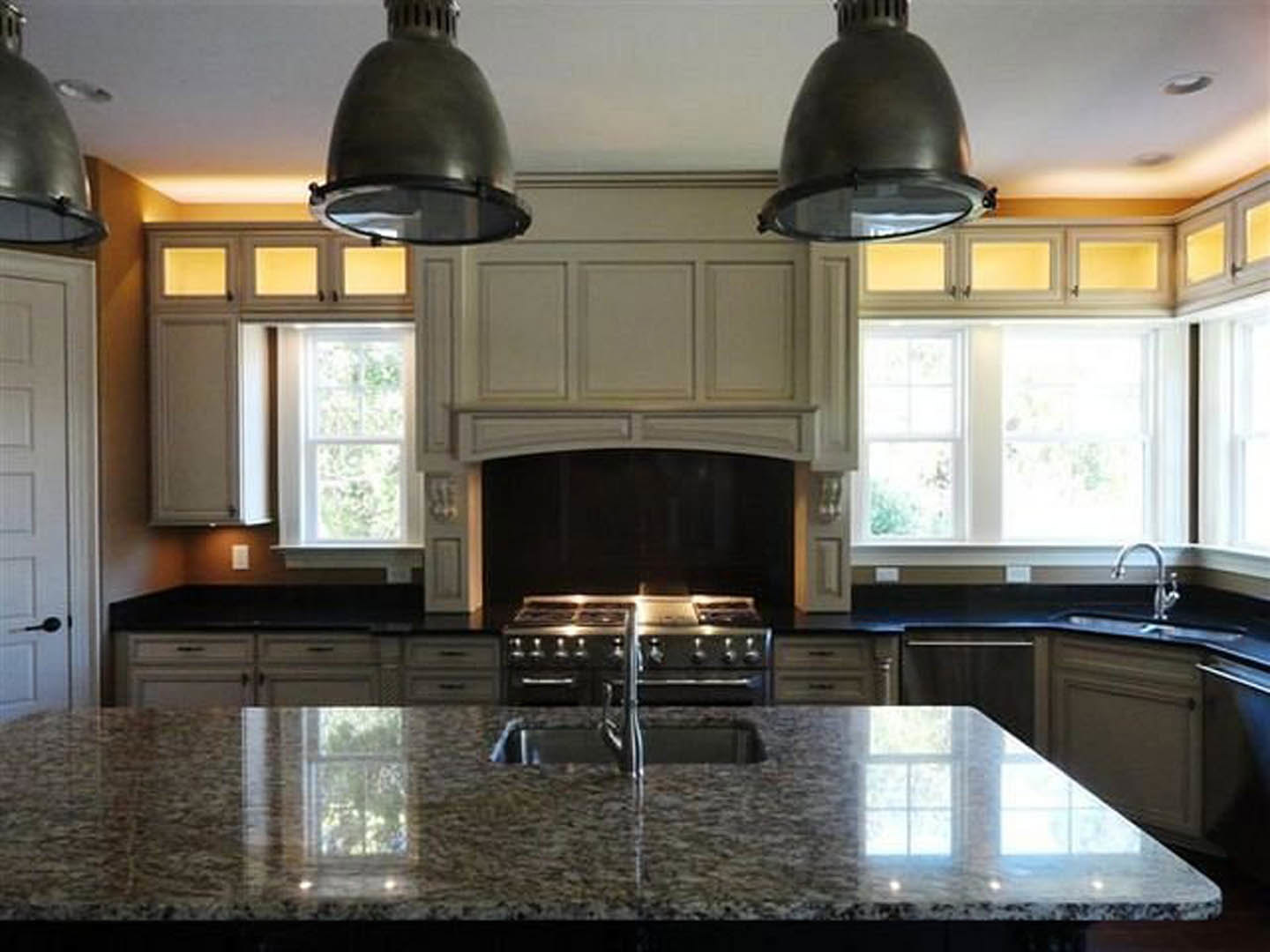 Marble kitchen island with built-in sink and chrome faucet, white cabinetry, pendant lights, stainless steel appliances, and large window
