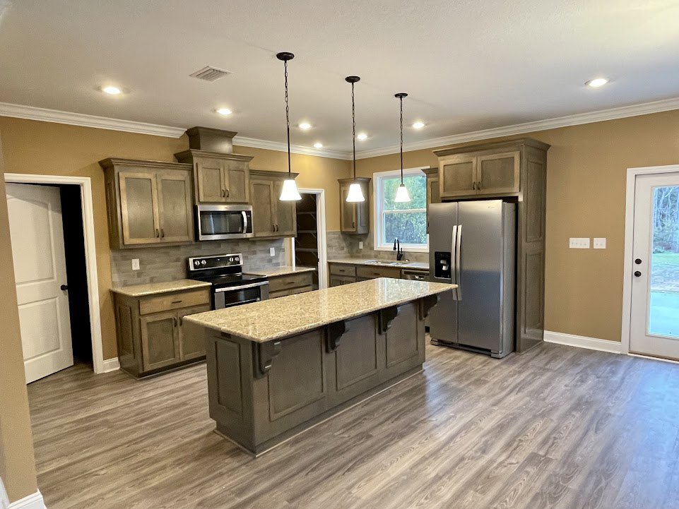Spacious kitchen featuring a marble-topped island, stainless steel refrigerator, black stove with wooden countertop, built-in microwave, white cabinetry, and a door with a window.