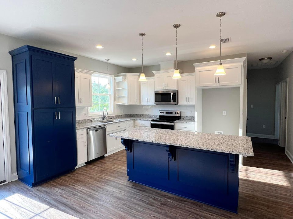 Marble kitchen island with waterfall edge, stainless steel refrigerator and stove, blue cabinets with silver handles, built-in microwave, light wood flooring, undermount sink
