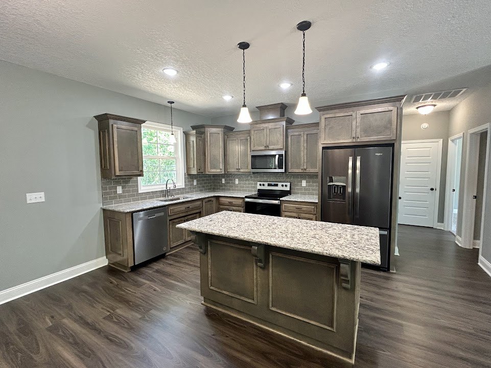 Kitchen with marble-topped island, black refrigerator with silver handles, black and white oven, tile flooring, white cabinetry, pendant lights, and window with light fixture.