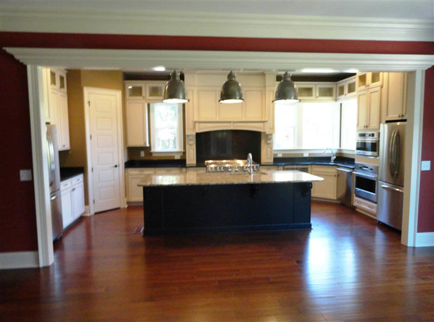 Spacious kitchen featuring a large central island with white countertops, stainless steel refrigerator, white cabinetry, and modern sink fixtures