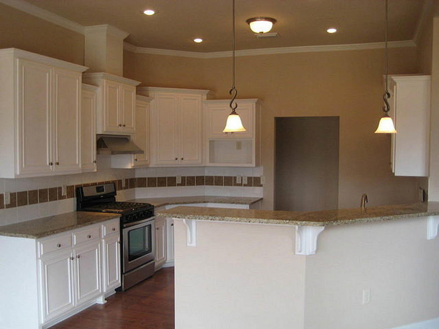 White shaker cabinets, marble countertop bar, stainless steel stove, bell-shaped pendant light fixture, neutral walls
