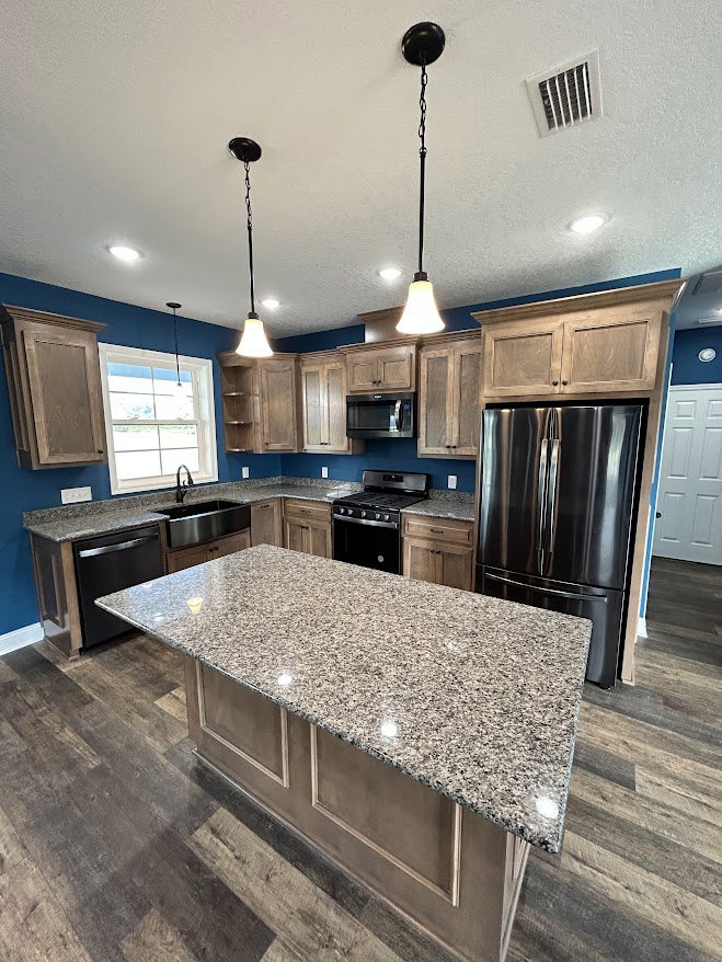 Granite kitchen island with marble countertops, stainless steel appliances including black refrigerator and stove, white cabinetry, window above sink, pendant light fixture