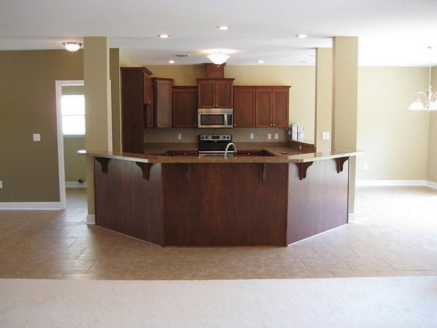 Open kitchen with white cabinetry, stone countertops, stainless steel appliances, built-in bar seating, and pendant lighting over the island