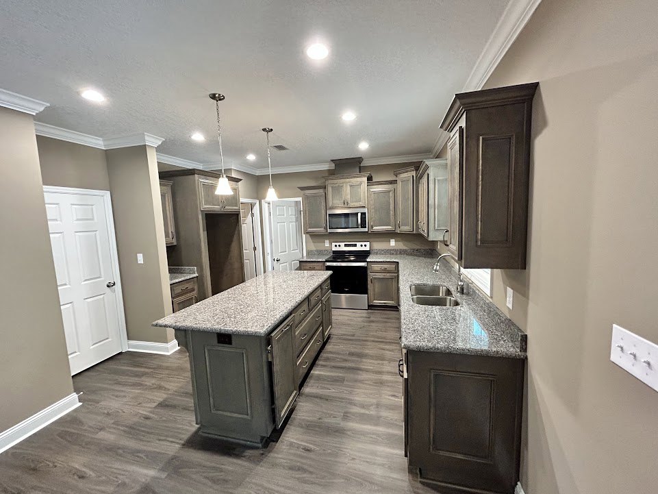 Granite countertops and wood flooring in a kitchen with a black and silver dishwasher, kitchen island featuring drawers and cabinet door, white door with silver handle, white light