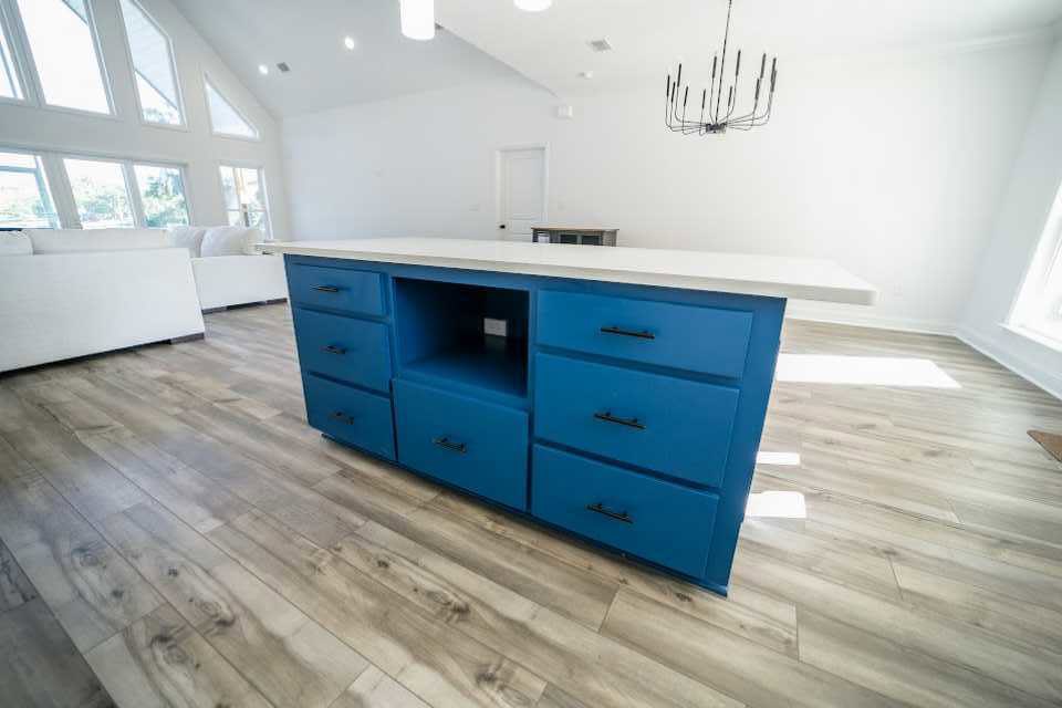 Blue and white kitchen island with blue cabinetry, black handles, white countertop, stainless steel sink, and large windows in a bright room