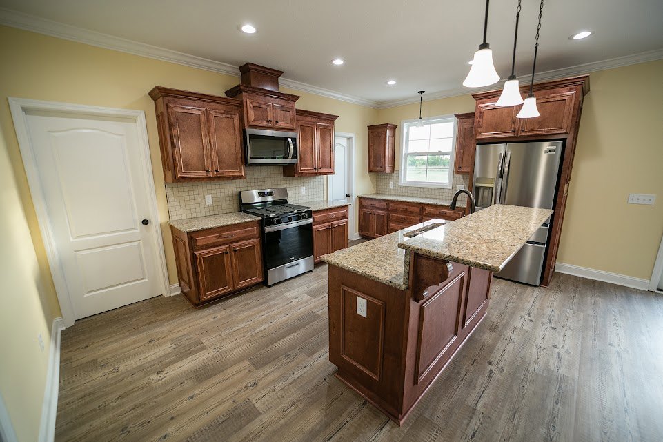 Granite kitchen island with stainless steel refrigerator, stove, and white cabinetry; close-up window and white door with black knob visible