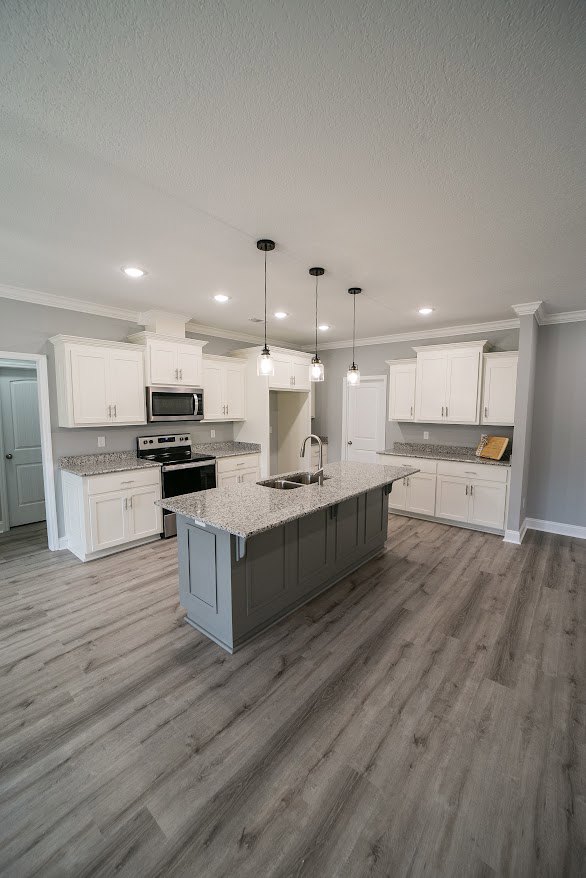Marble kitchen island with built-in sink, surrounded by white cabinetry and stainless steel appliances, light wood flooring, and recessed lighting