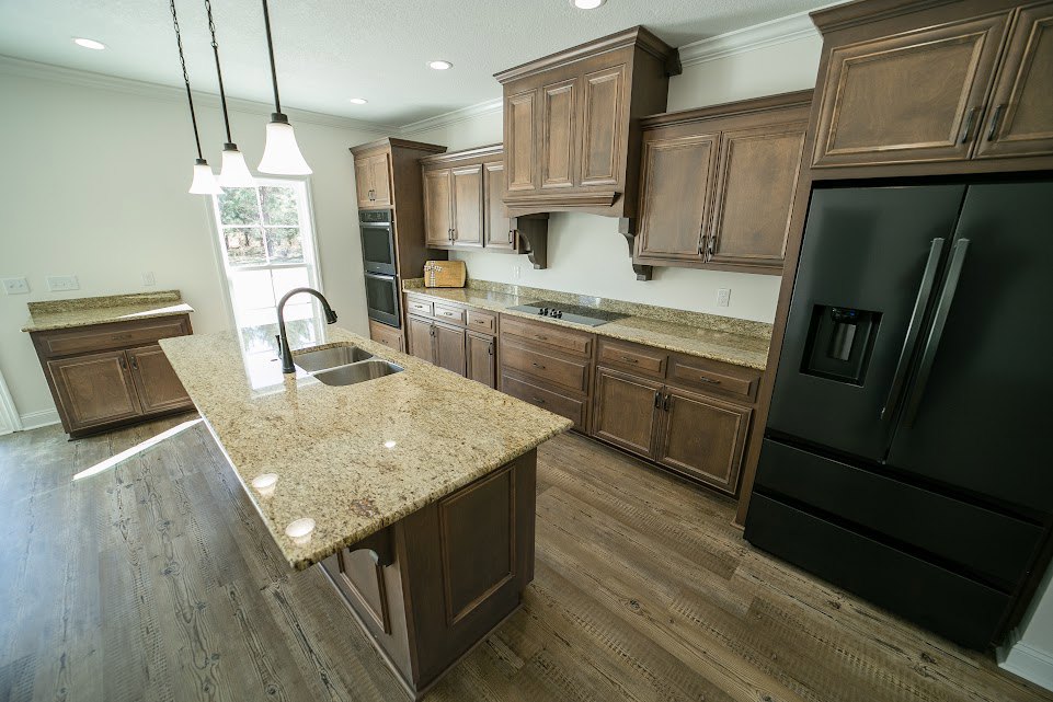Kitchen featuring black refrigerator with water dispenser, granite countertops, wooden cabinetry, kitchen island with sink, and row of pendant lights