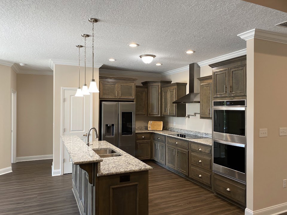 Marble countertop kitchen with stainless steel stove, kitchen island sink, stainless steel oven, refrigerator, cabinetry, and ceiling-mounted chain lighting