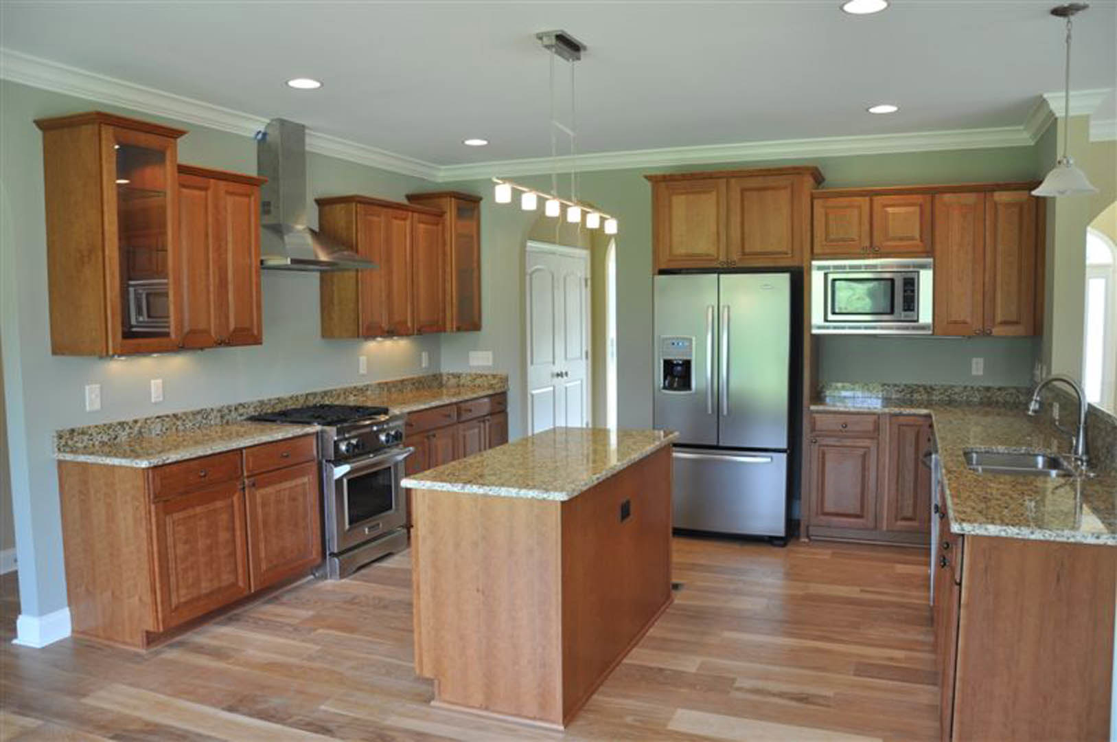 Kitchen with light wood cabinets, marble-topped island, stainless steel appliances, and polished countertops