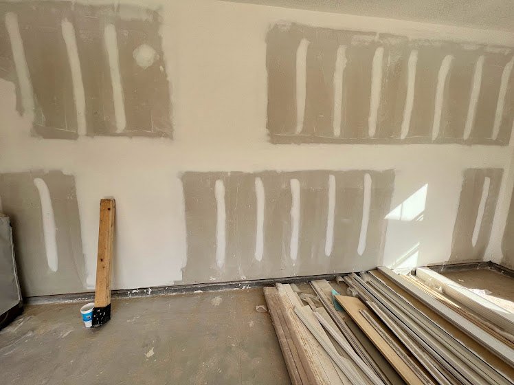 Room under construction with plastered wall and stacked wood planks on unfinished floor