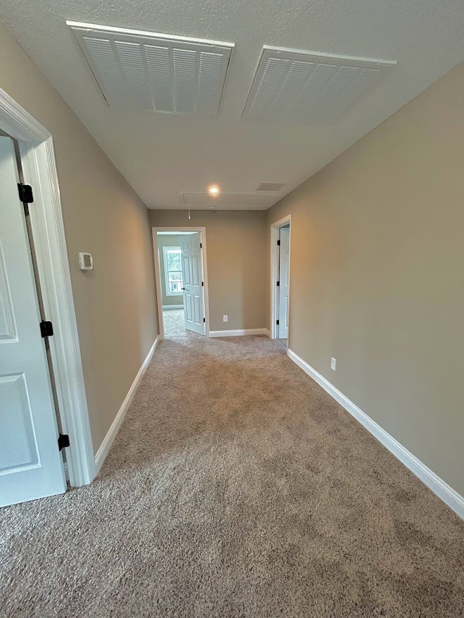 Hallway with beige carpet, white paneled doors featuring black handles, white walls, and ceiling with rectangular vent cover