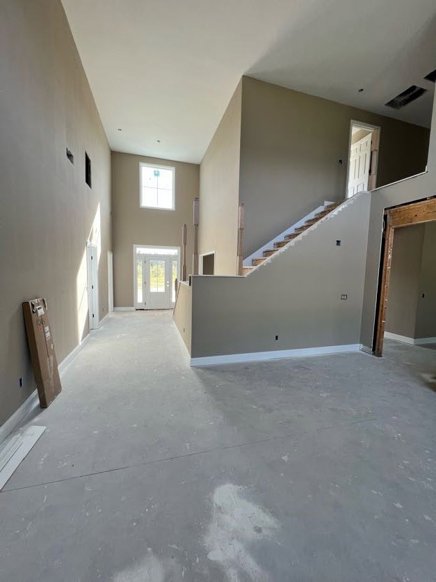 White staircase with brown wooden steps, white door with glass panes, unfinished walls, window with square sign, white floor, brown box with white labels in a house under