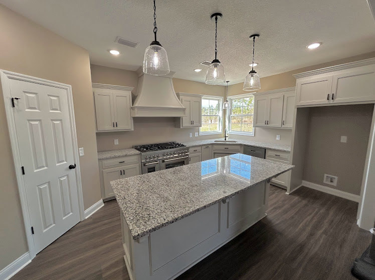 Marble island with waterfall edge, stainless steel stove, white tile backsplash, light wood cabinetry, undermount sink, and hardwood flooring