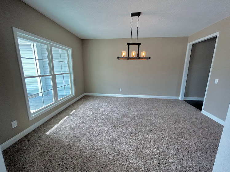 Neutral-toned carpeted room with white walls, ceiling-mounted light fixture, crown molding, and wood trim