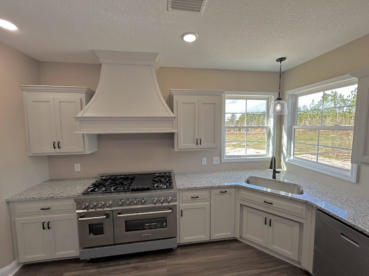 White kitchen cabinets, large stainless steel stove, light countertops, tile backsplash, and overhead range hood