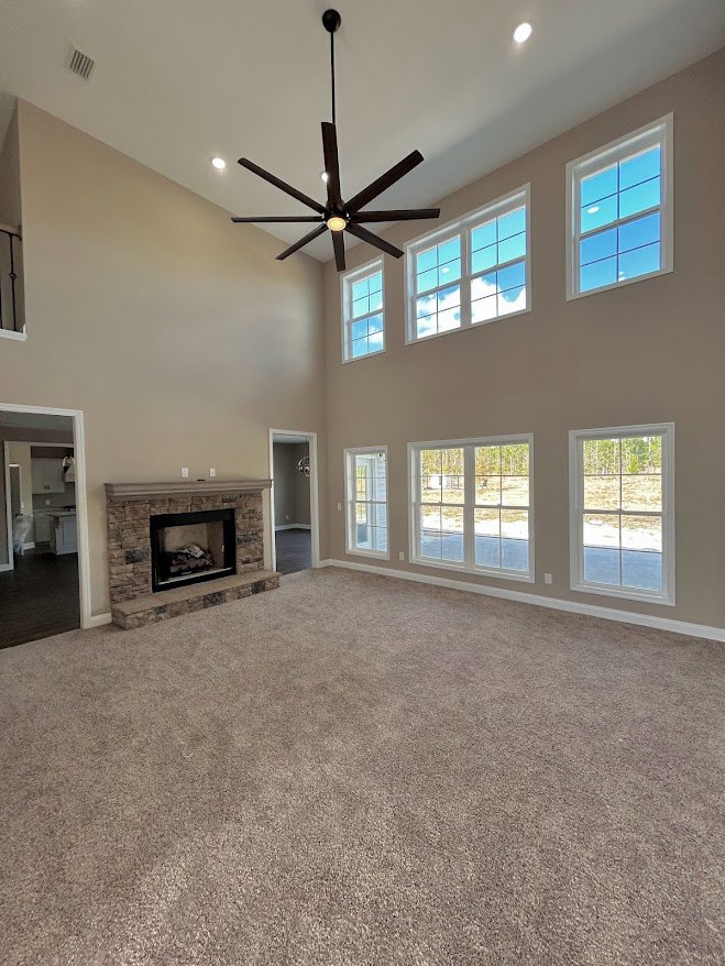 Living room featuring stone-surround fireplace with black frame, ceiling fan with light, large window overlooking open field, neutral walls and flooring