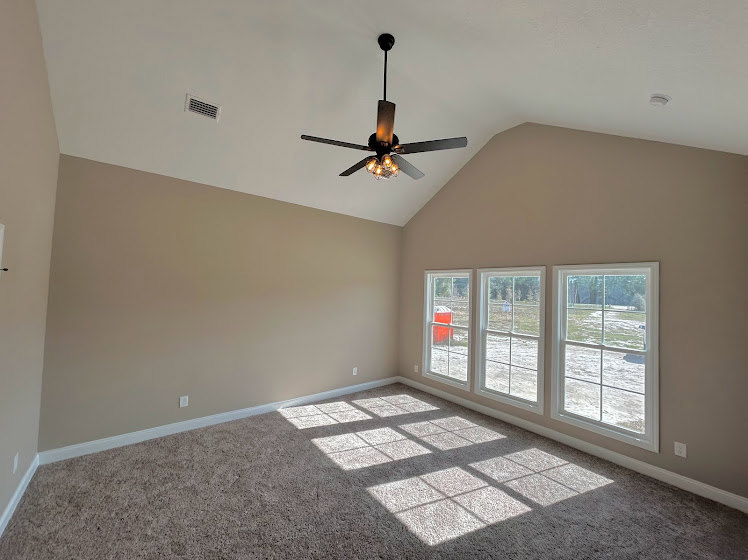 Ceiling fan mounted on white plaster ceiling, large windows with trim, neutral walls, hardwood flooring