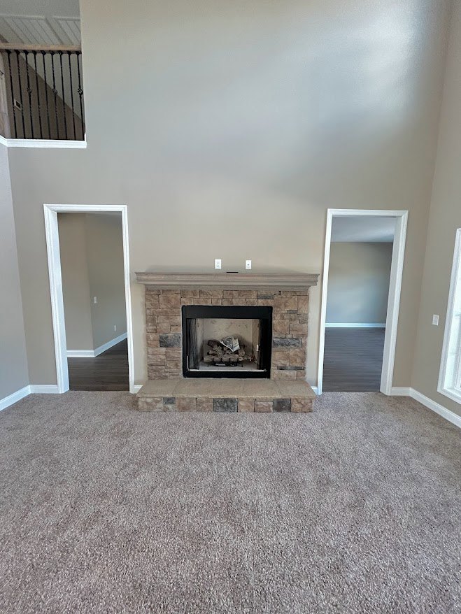 Stone fireplace with glass door, white mantel, built-in cabinetry, carpeted floor, doorway leading to adjacent room