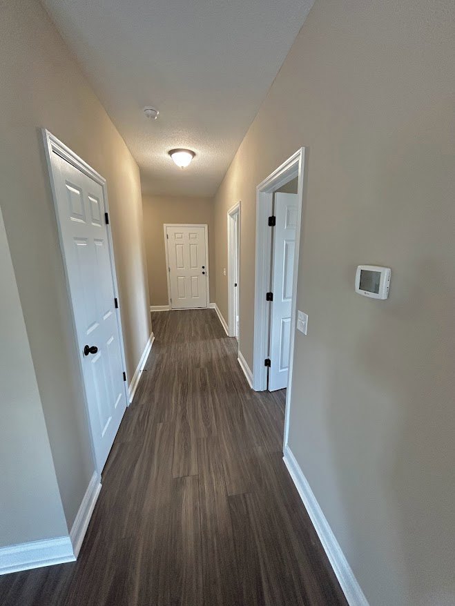 Hallway with white paneled doors, black hardware, wood plank flooring, and white plaster walls