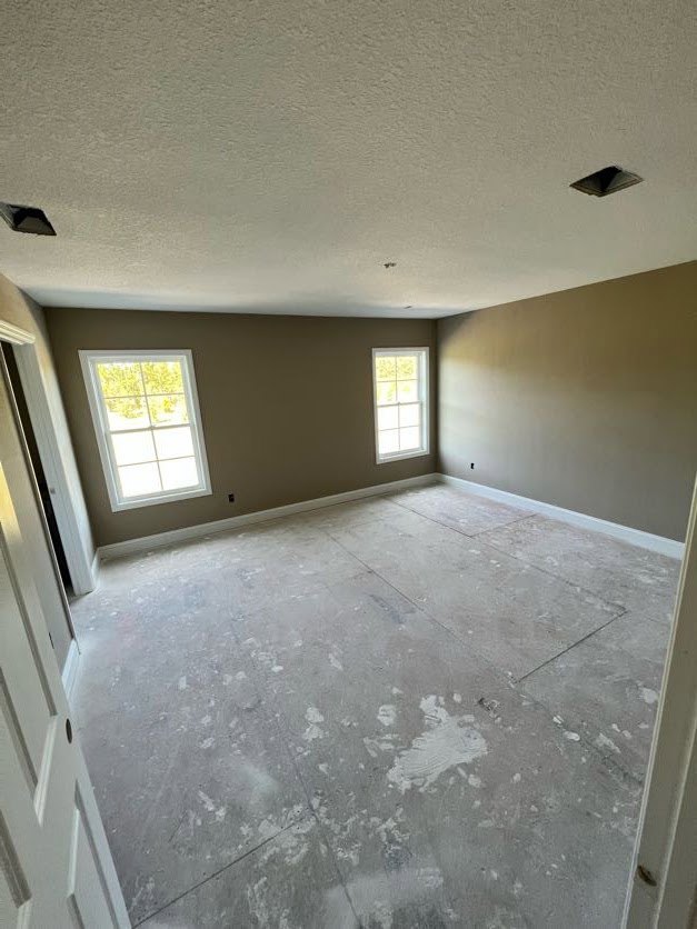 Bright room with white ceiling, large windows with white frames, tile flooring, white door, and plaster walls