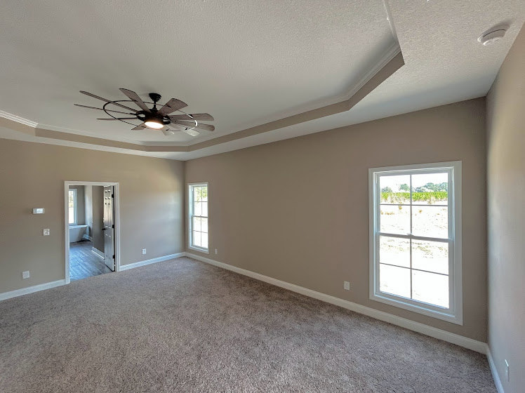 Bright room with light-colored plaster walls, wood flooring, ceiling fan with integrated light, and large windows allowing natural daylight