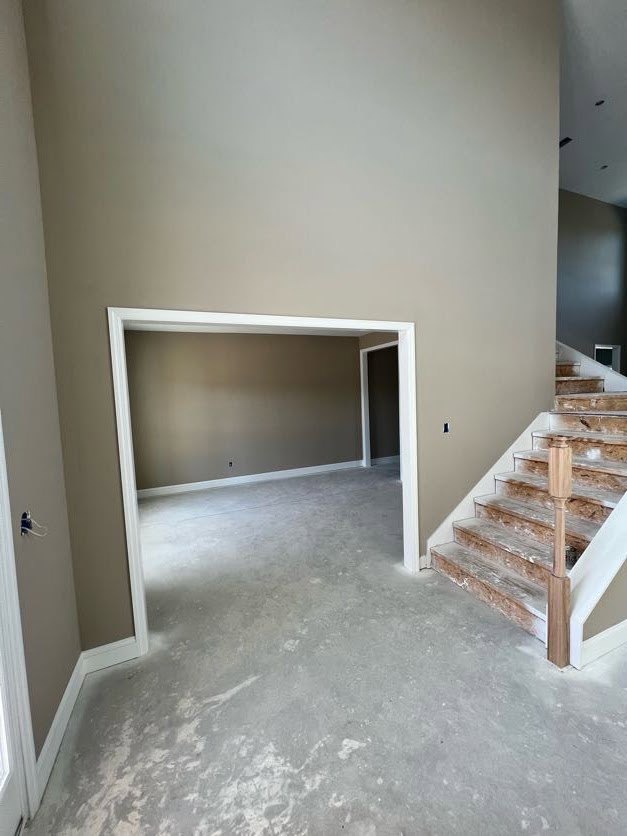 Modern staircase with wood steps and white railing, concrete floor, grey wall with white trim, and white door frame in a residential interior.