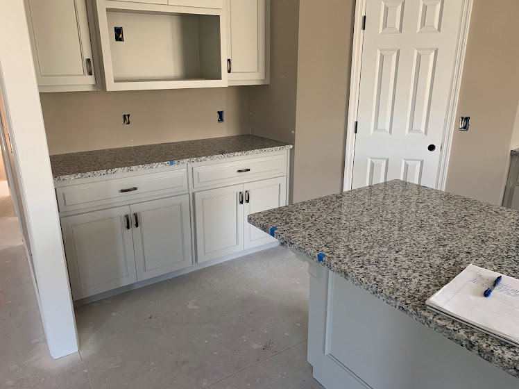 White kitchen cabinets with polished granite countertops, stainless steel faucet, tile backsplash, and a marble island featuring a notebook and pen.