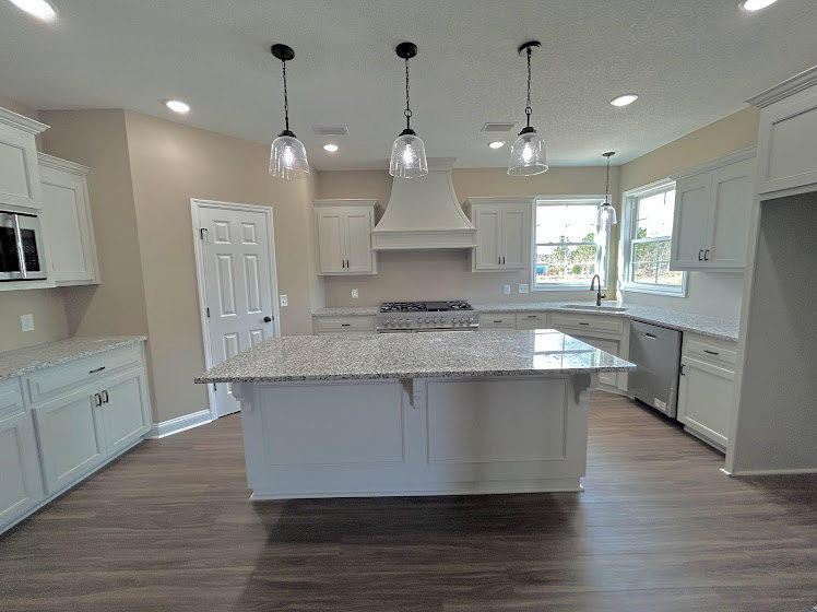 Spacious kitchen featuring a large white island with gray countertop, white cabinetry, stainless steel sink, pendant light fixtures, and hardwood flooring