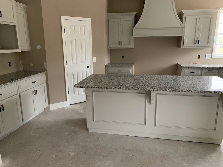 Granite kitchen countertops with white cabinetry, black hardware, stainless steel sink, and white door