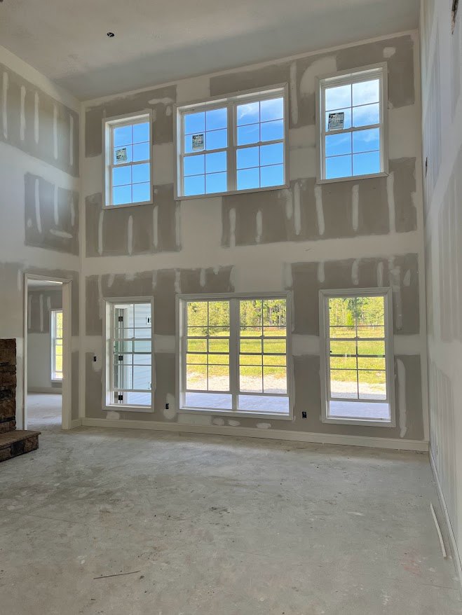 Spacious room featuring large windows with views of grass and trees, polished concrete floor, white door frame set in a stone wall, plaster walls, and a window with a sticker on