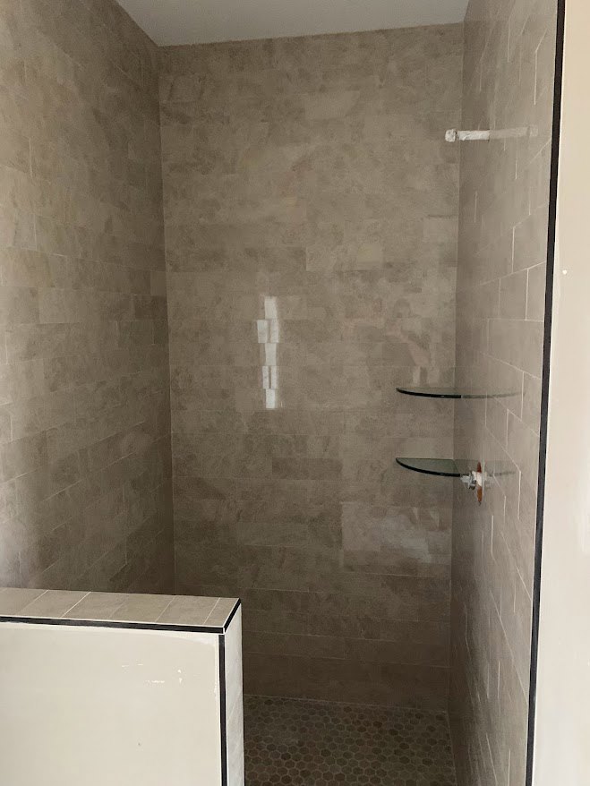 White tile shower with black border, glass shelf mounted on wall, chrome plumbing fixtures, plaster ceiling