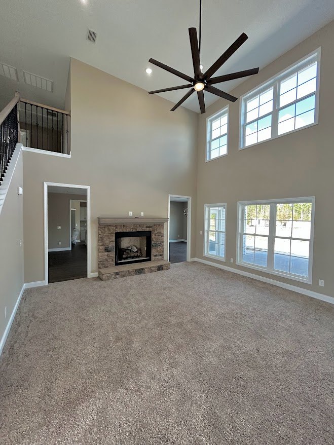 Living room featuring a stone-surround fireplace with black frame, ceiling fan with lights, white walls, window with white trim, and light fixture.