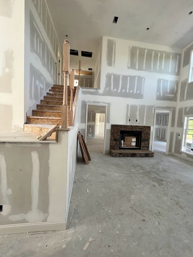 Wood staircase with white risers and handrail, adjacent to a brick fireplace containing a cardboard box, white painted walls, doorway, and ceiling visible in a modern interior.