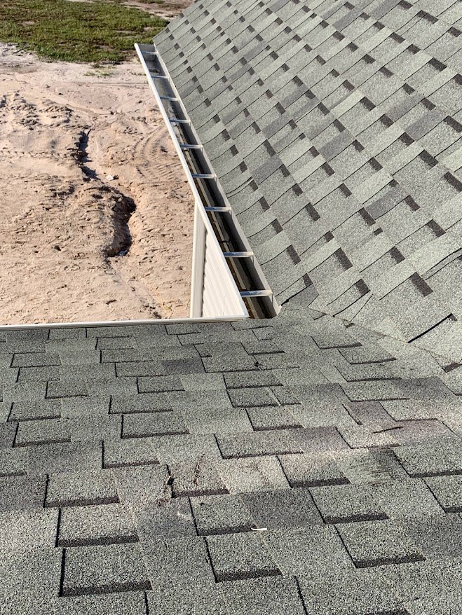 Dark gray shingle roof with white gutter above red brick exterior, concrete walkway, and flagstone ground.