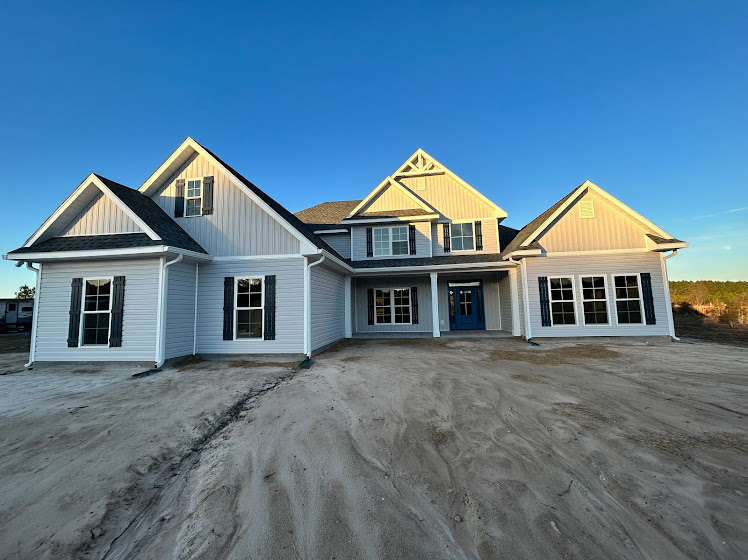 White siding home with blue front door, black shuttered windows, white window frames, gabled roof, and dirt landscaping under a clear blue sky