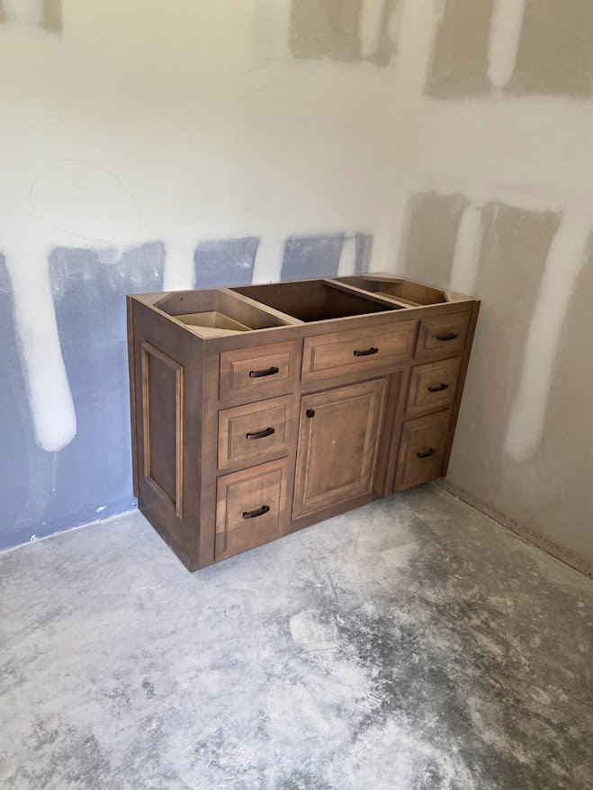 Wood kitchen cabinet with multiple drawers, silver handles, white painted walls, and light hardwood flooring