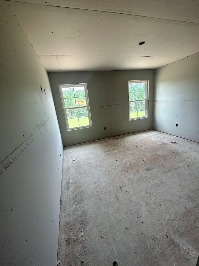 Spacious room with two large square windows, polished concrete floor, white plaster walls, and ceiling fixture; faint writing visible on wall.