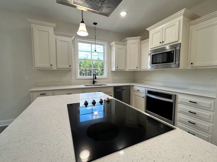 White kitchen cabinets, black stove with oven, built-in microwave above, light-colored countertop, stainless steel sink, neutral wall backdrop