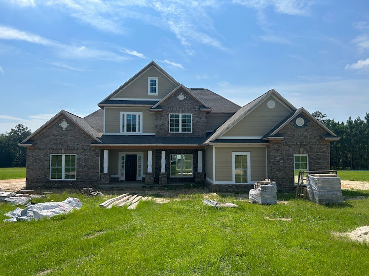Modern home under construction with white-framed windows, black front door, and large entryway, set on grassy yard beneath clear blue sky